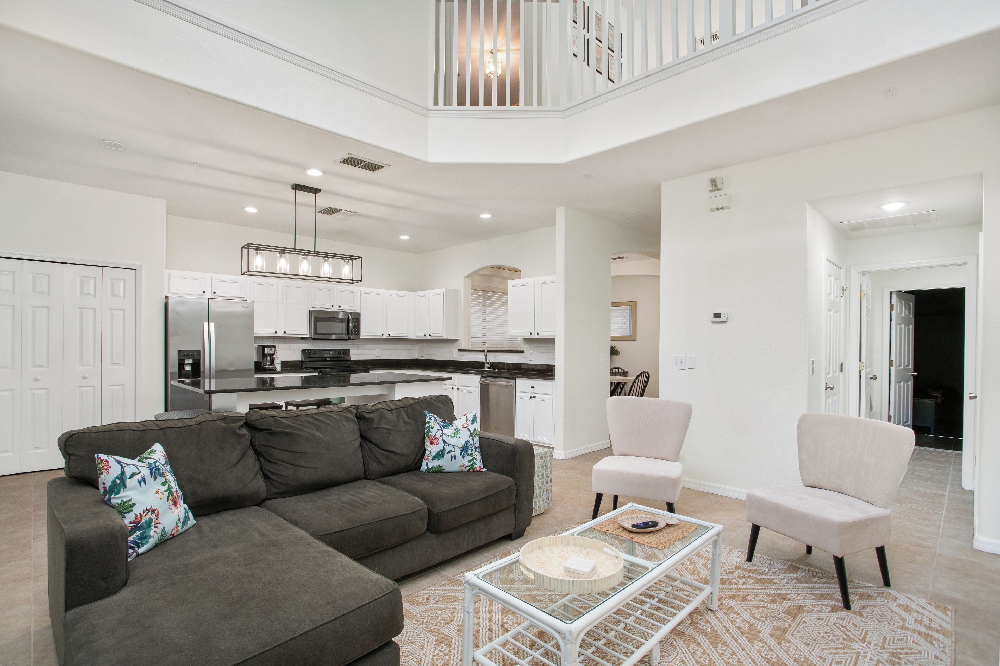 A modern living room with a gray sectional sofa, a glass coffee table, and a white accent wall.