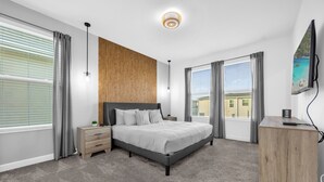 Ett modernt sovrum med en stor säng, en väggpanel i trä, grå gardiner och utsikt över en byggnad genom fönstret.