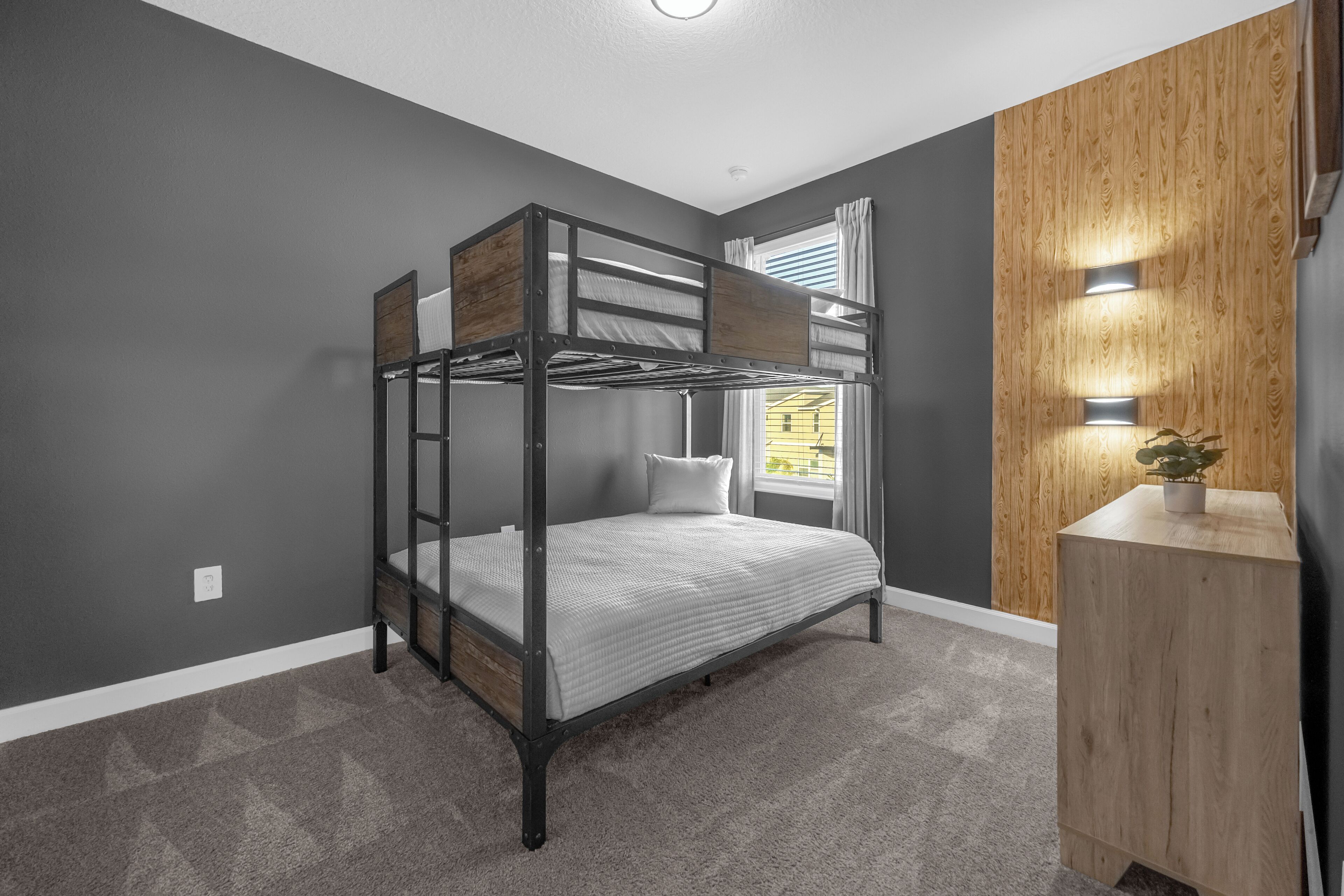 A bunk bed in a room with grey walls, a wooden cabinet, and a window with curtains.