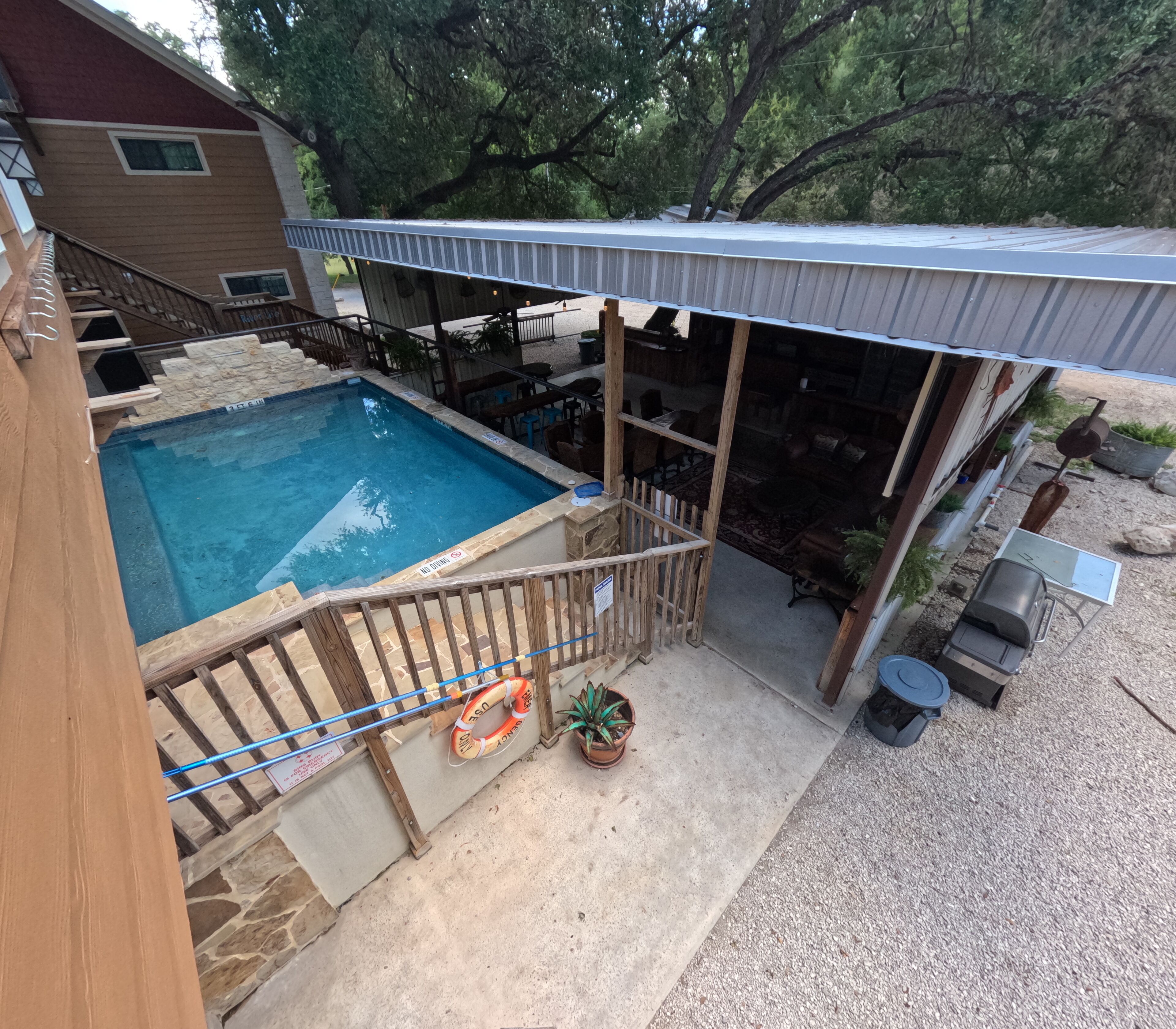 A backyard with a swimming pool, wooden deck, outdoor seating, and a covered patio area.