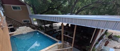 A backyard with a swimming pool, wooden deck, outdoor seating, and a covered patio area.