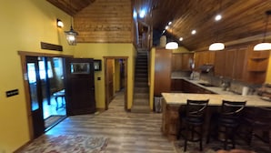 Une cuisine spacieuse avec des poutres apparentes en bois au plafond, un îlot central doté de tabourets de bar et une vue sur la salle à manger.