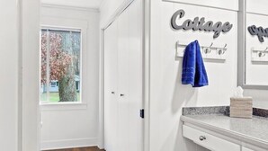 Un pasillo con una puerta que da a una habitación, una ventana con vista a un árbol y un perchero de pared con una toalla.