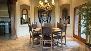 Un espace repas comprenant une table ronde, des chaises, un lustre et un grand miroir.