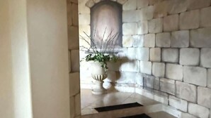 Une cheminée en pierre ornée d’une plante sur le manteau, un mur blanc et un sol carrelé.