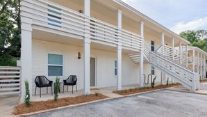 A building with a white brick exterior, multiple balconies, and a covered outdoor seating area with chairs. - Newly Decorated BEAUTY in Downtown Ocean Springs with optional GOLF CART. (Ocean Springs)