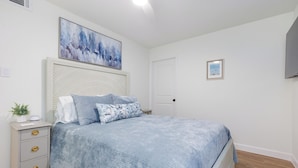 A bedroom with a bed, a nightstand, a wall-mounted TV, and a door. - Newly Decorated BEAUTY in Downtown Ocean Springs with optional GOLF CART. (Ocean Springs)