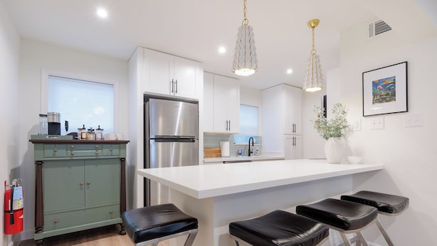 A modern kitchen with a stainless steel refrigerator, white cabinetry, and a central island with bar stools. - Newly Decorated BEAUTY in Downtown Ocean Springs with optional GOLF CART. (Ocean Springs)