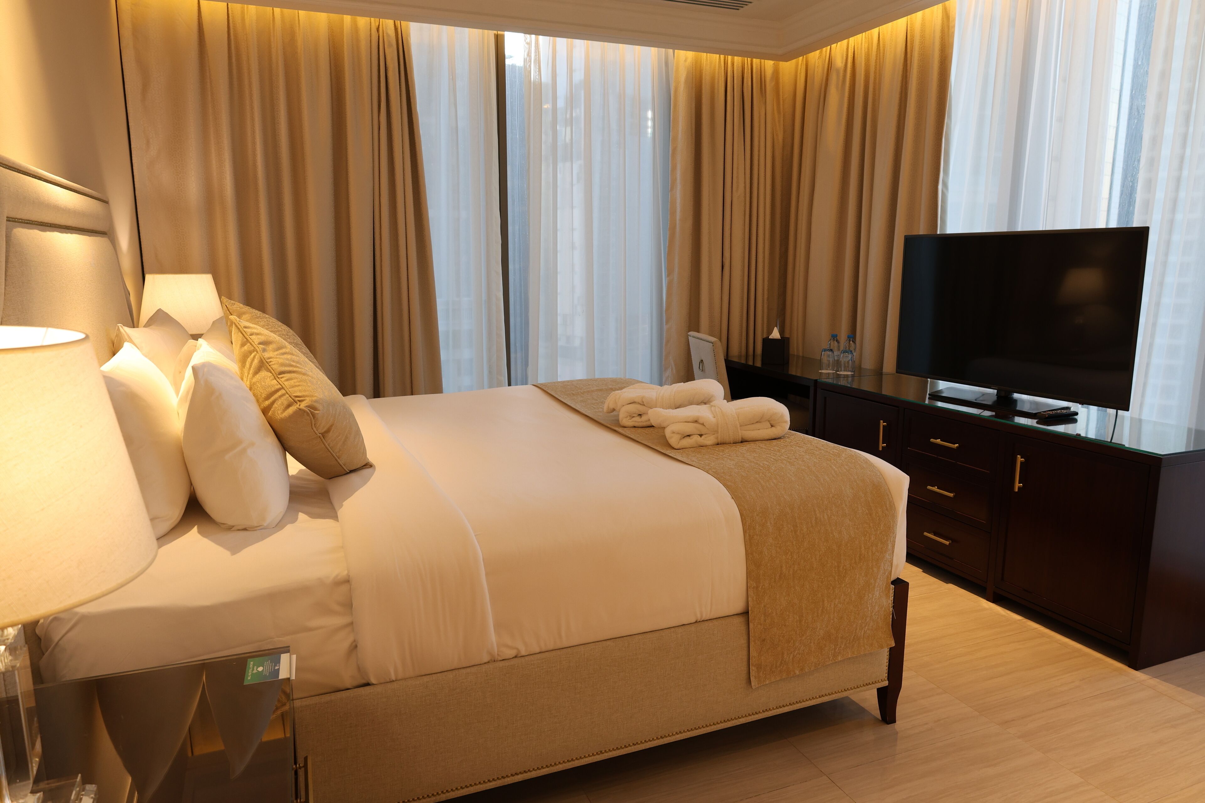 A hotel room with a large bed, a flat-screen TV, a bedside table with a lamp, and a dresser.