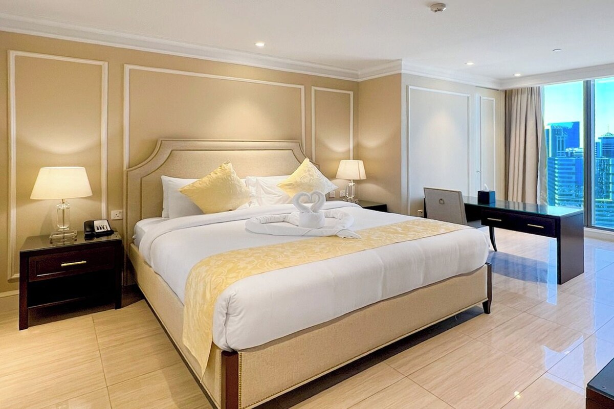 A hotel room with a large bed, bedside tables, a desk, and a city view.