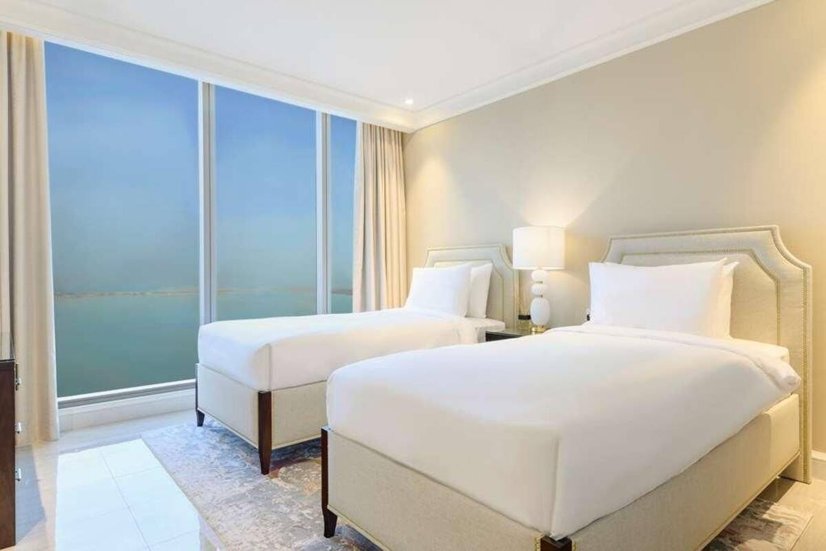 Habitación de hotel con dos camas, un ventanal con cortinas y vista al mar.