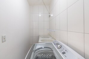 A compact laundry room with a front-loading washing machine, a small sink, and tiled walls.