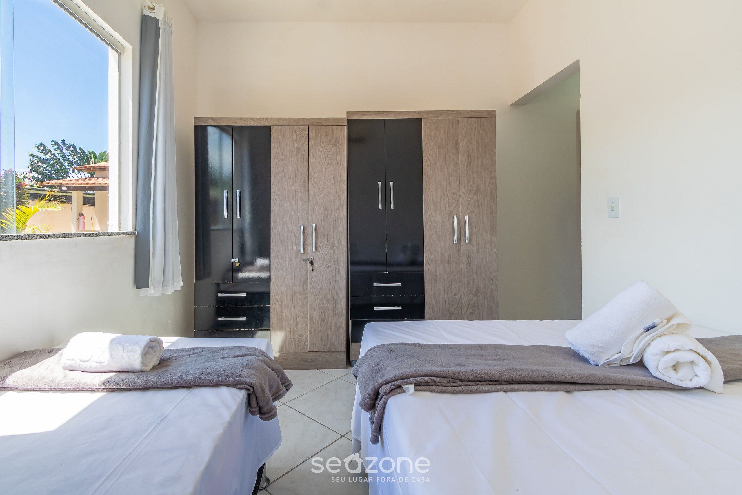 Quarto de hotel com duas camas, um guarda-roupa e uma janela com cortinas.