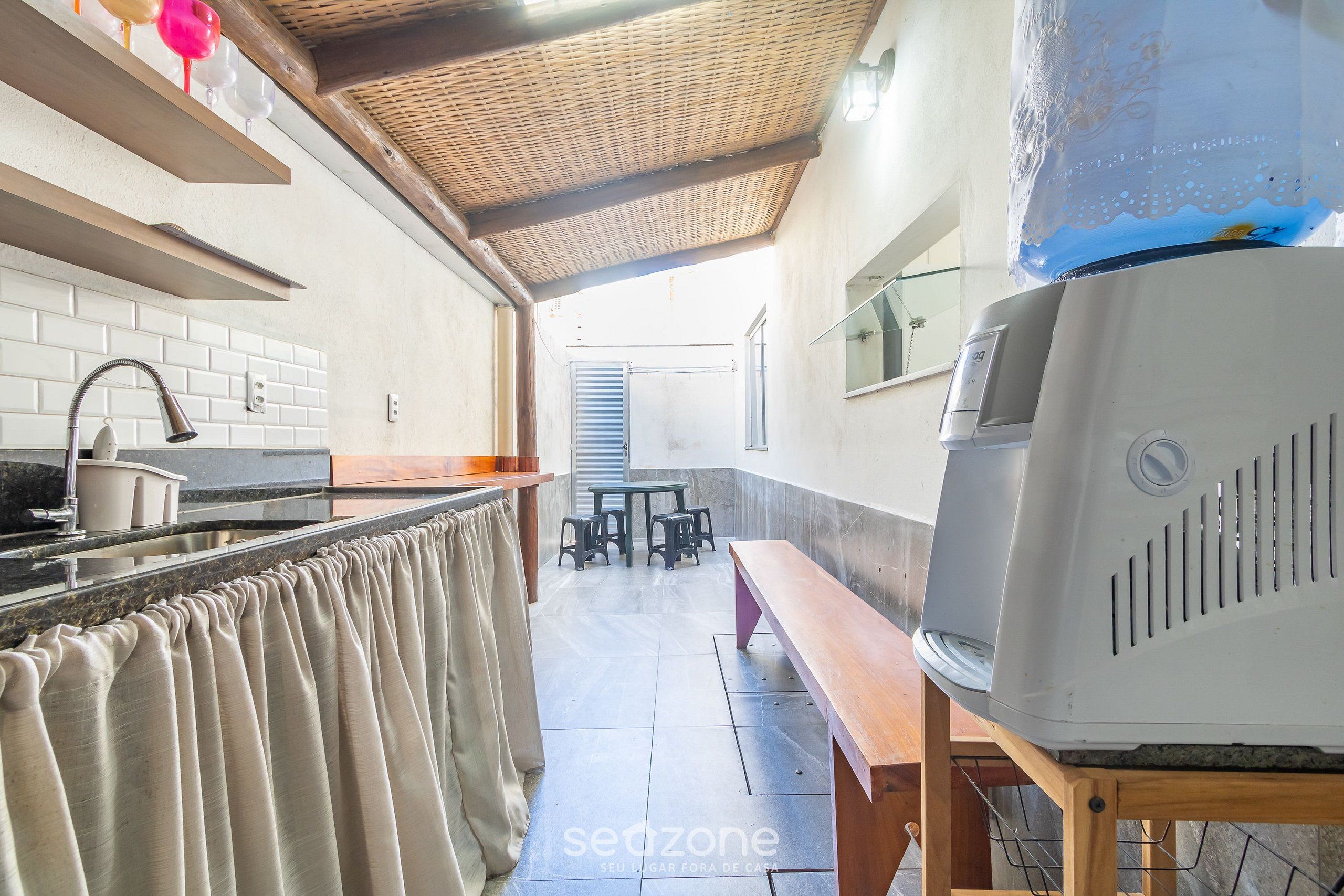 A kitchen with a tiled backsplash, a wooden bench, a grill, and a dining area with stools.