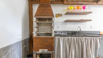 A kitchen with a wooden chimney, a hanging shelf with colorful glasses, and a sign reading "Cantinho Dachwrass".