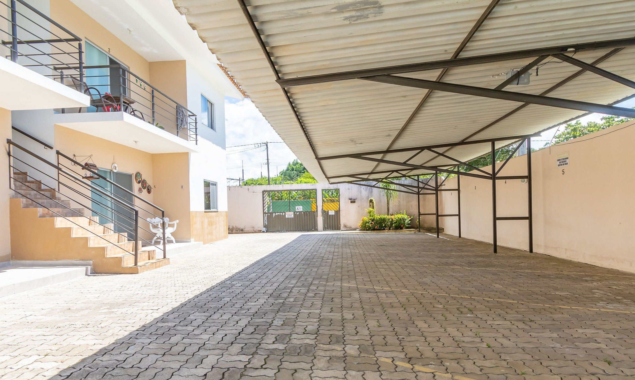 A covered outdoor area with a paved walkway, a staircase, and a gated entrance.