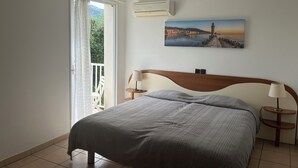 A bedroom with a bed, a window with curtains, a painting on the wall, and an air conditioning unit. - The Maristella and Argentu villas for large families close to the sea (Aregno)