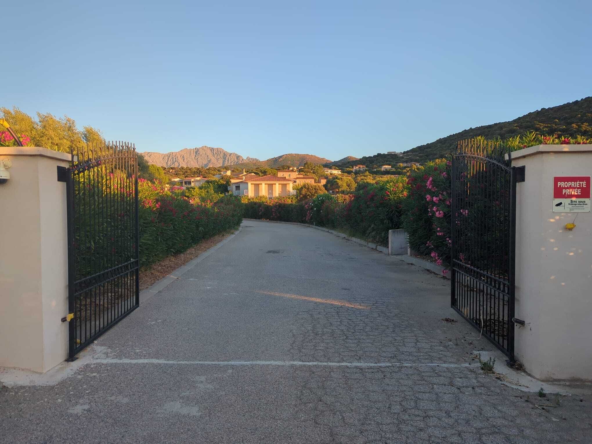 A gated driveway leading to a building with a mountainous backdrop.