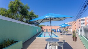 A rooftop pool area with blue umbrellas, a pool, and a seating area with chairs and a table. - PDC - Apartments in a Condominium With a Pool in Ilheus (Ilhéus)