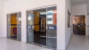 A fitness center with glass doors, exercise equipment, and a sign for 'Praias de Atalanta'. - PDC - Apartments in a Condominium With a Pool in Ilheus (Ilhéus)