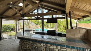 Ein überdachter Außenbereich mit einer Steinsitzbank, einem Pool und einem Grill.
