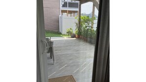 A view through a glass door of a patio area with a welcome mat, a bench, and potted plants.