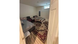 A small, compact room with a bed, a desk, and a chair. There is a window providing natural light and a door leading to another room.