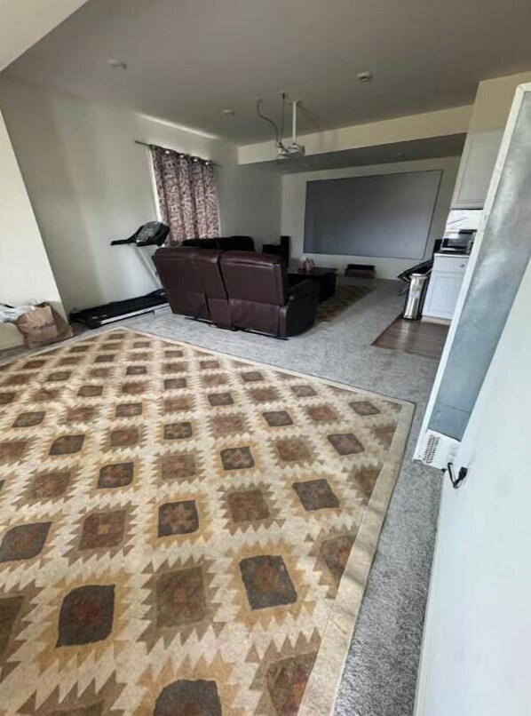 A living room with a patterned carpet, a sofa, a television, and a kitchen area.