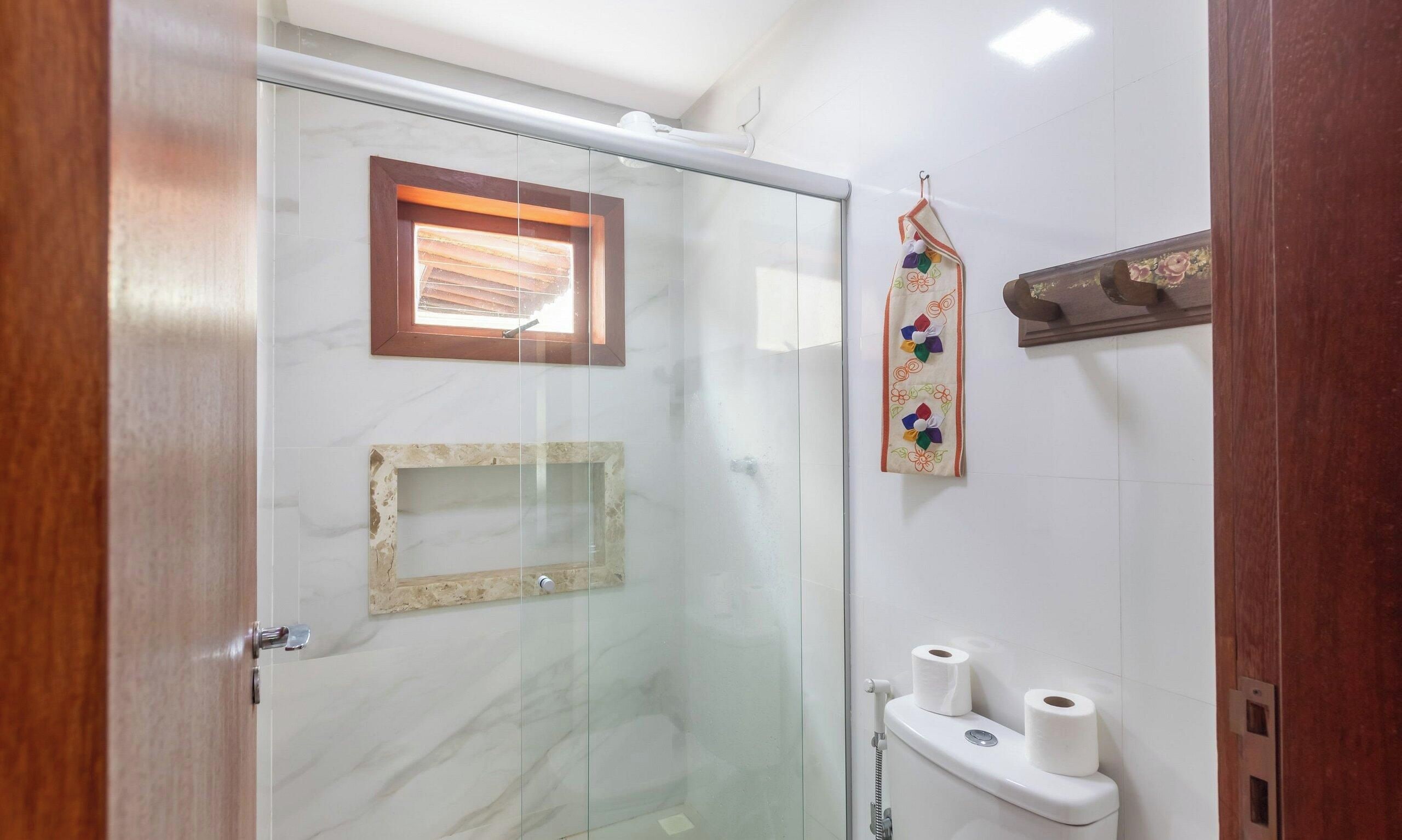 A glass-enclosed shower area with a wooden door, a small window, and a towel rack with a floral pattern.