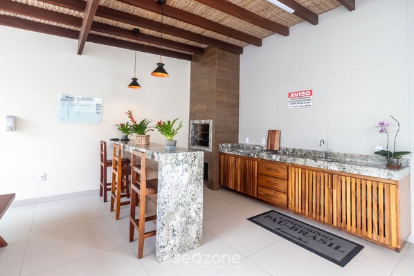 A kitchen with a marble island, wooden chairs, pendant lights, and a backsplash.