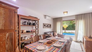 A dining area with a checkered tablecloth, wooden cabinets, and a view of a swimming pool. - House w/ Pool 180m From Beach in Arraial Pbr0003 (Porto Seguro)