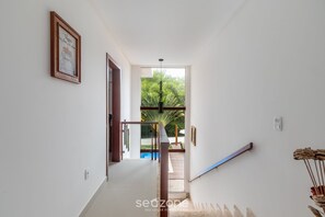 A hallway leading to a balcony with a glass door, a framed picture on the wall, and a ceiling light. - House w/ Pool 180m From Beach in Arraial Pbr0003 (Porto Seguro)