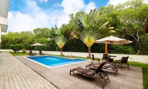 A swimming pool with lounge chairs and umbrellas, surrounded by greenery and a fenced area. - House w/ Pool 180m From Beach in Arraial Pbr0003 (Porto Seguro)