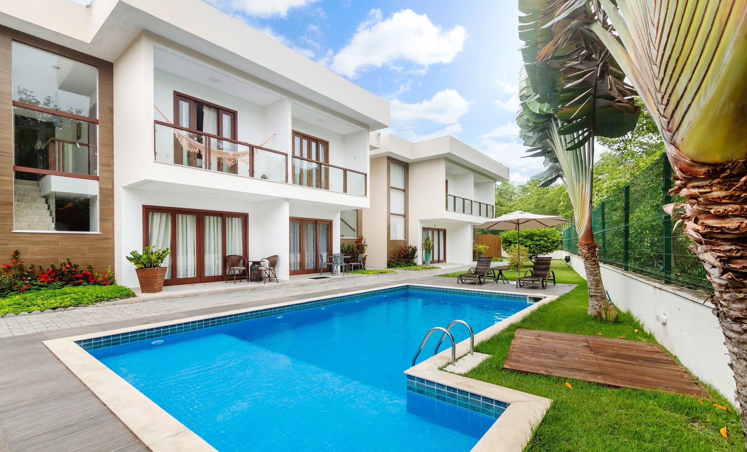 A modern two-story house with a swimming pool, outdoor seating, and a well-maintained garden.