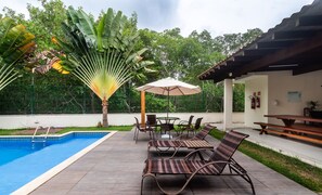 A poolside area with a pool, lounge chairs, and an umbrella. - House w/ Pool 180m From Beach in Arraial Pbr0003 (Porto Seguro)