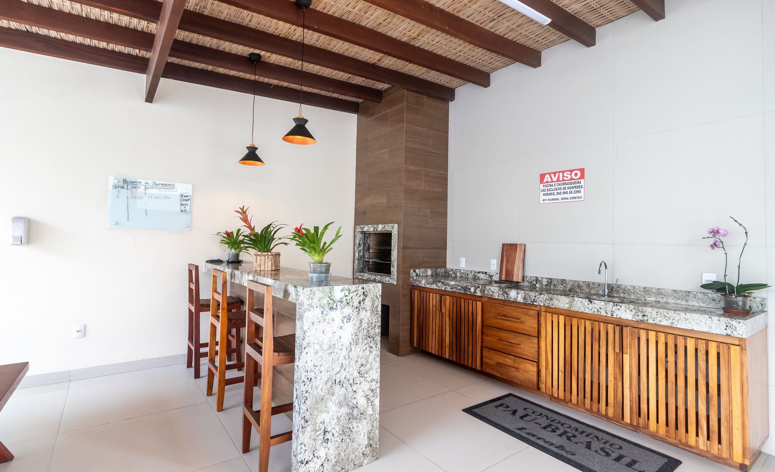 A kitchen with a marble island, wooden chairs, pendant lights, and a backsplash.