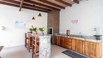 Uma cozinha com ilha de mármore, cadeiras de madeira, luminárias pendentes e painel atrás do fogão.