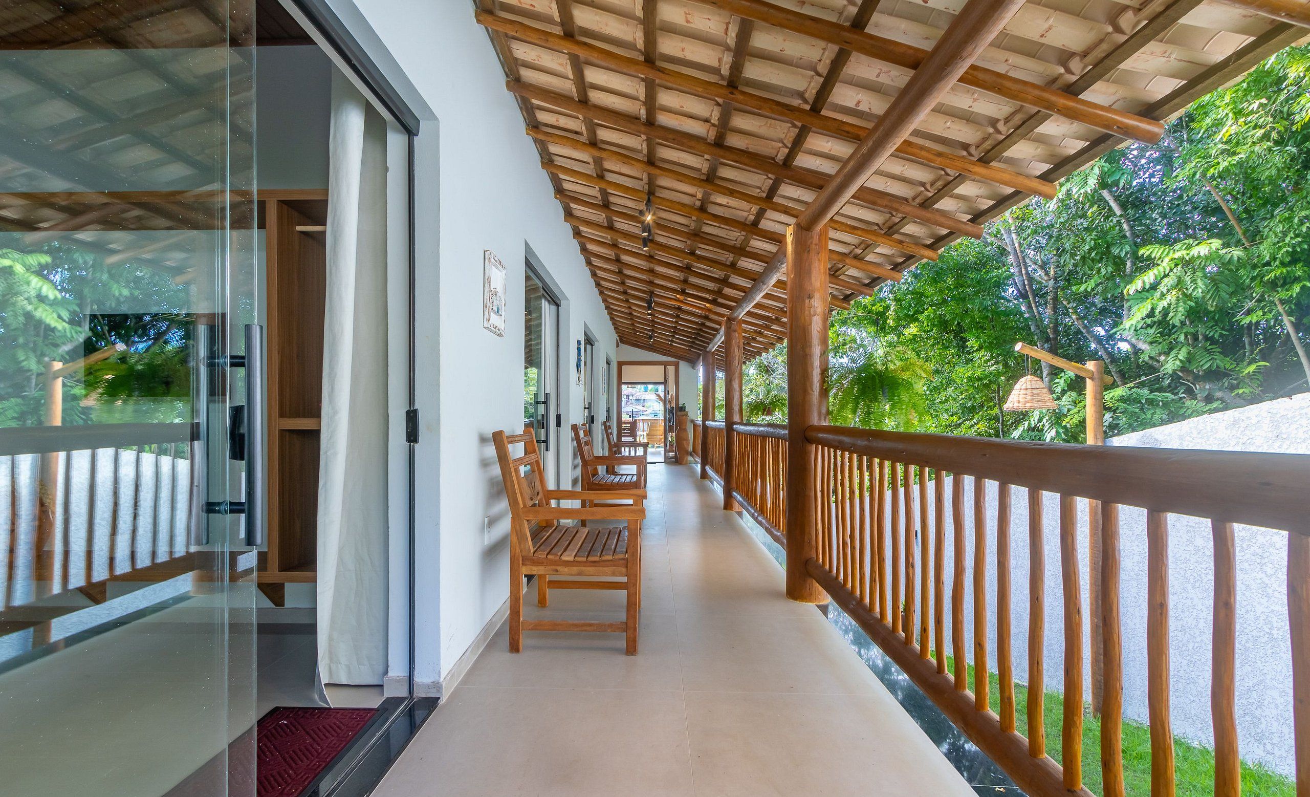 A covered corridor with wooden benches and a railing, leading to a door.