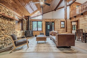 Ein Blockhaus-Interieur mit Steinwand, Holzbalkendecke, Kamin, einer Couch und einem Esstisch.