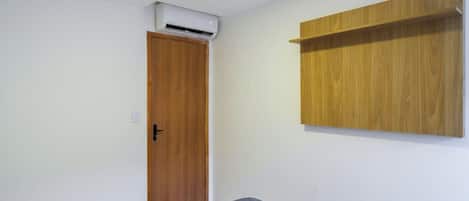 A room with a wooden door, an air conditioning unit above it, and a wooden shelf on the wall.