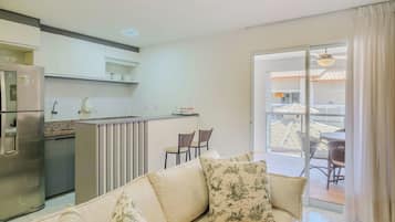 A modern kitchen with a refrigerator, a dining area with chairs, and a sofa with decorative pillows.