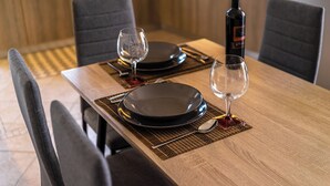 A dining table set with black plates, two wine glasses, a bottle of wine, and a spoon on a woven placemat.