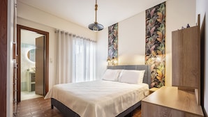 A modern bedroom with a large bed, wooden flooring, a built-in wardrobe, and a bathroom visible through an open door.