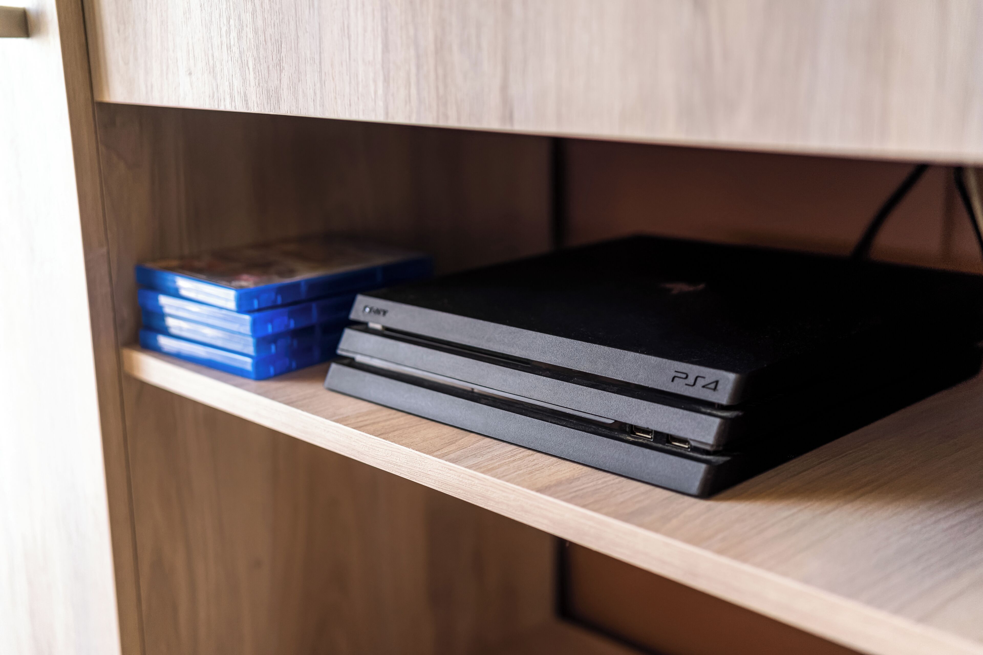 Une étagère en bois sur laquelle se trouve une console PlayStation 4 et une pile de boîtiers de jeux bleus.