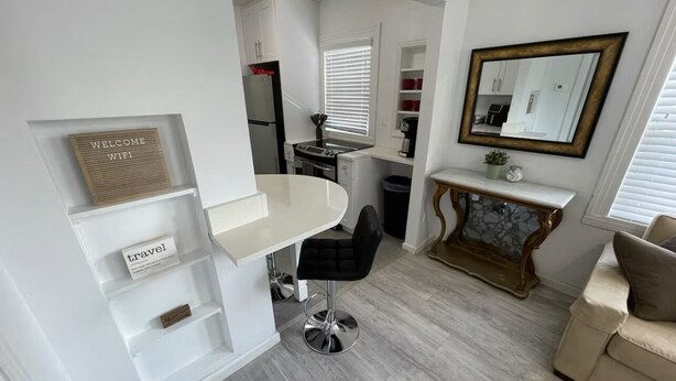 A compact kitchen with white cabinetry, a black bar stool, and a marble console table.