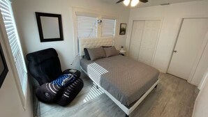 A bedroom with a bed, a chair, a ceiling fan, and a window with blinds.