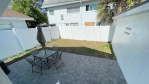 A patio with a table and chairs, a covered umbrella, and a white fence.