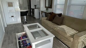 A modern living room with a glass coffee table, a beige sofa, and a kitchen in the background.