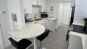 A compact kitchen with white cabinets, a round dining table with two black bar stools, a microwave, and a refrigerator.