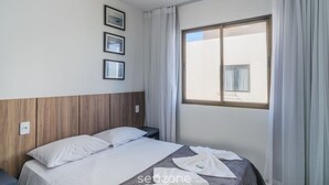 Una habitación de hotel con una cama, una mesita de noche, una ventana con cortinas y tres cuadros en la pared.